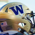 A row of three gold UW football helmets at a football game at Husky Stadium.