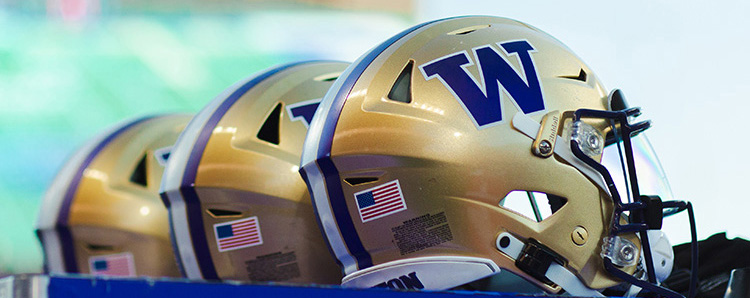 A row of three gold UW football helmets overlooks at UW football game at Husky Stadium.